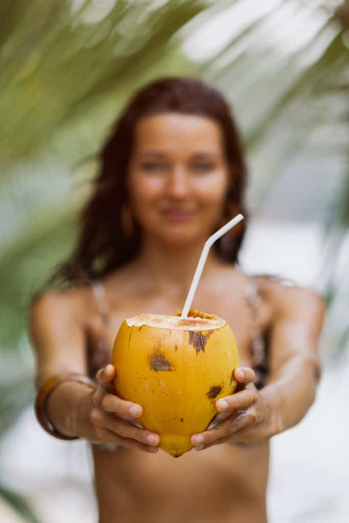 Frau im Bikini hält Kokosnuss mit Strohhalm am Strand